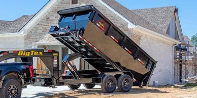 A black Big Tex dump trailer attached to a truck at a construction site.