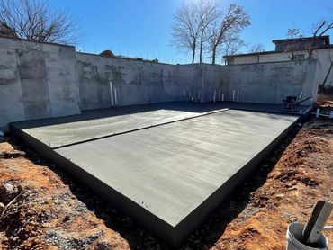 Newly poured concrete foundation slab for a building under clear blue sky.