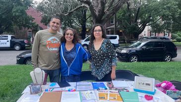 Three people standing behind a table with papers outdoors.