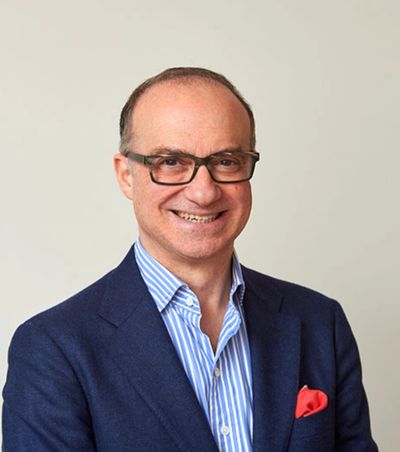 Smiling man in glasses wearing a blue blazer and striped shirt.