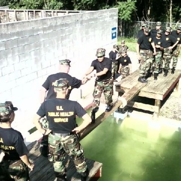 Group of uniformed personnel crossing a water obstacle on wooden planks.