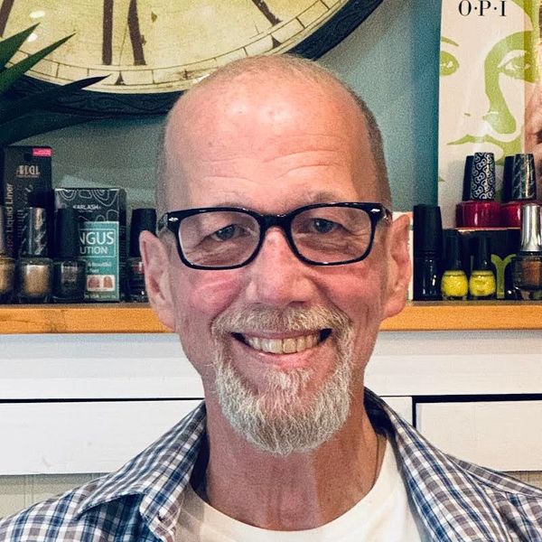 Smiling elderly man with glasses and a goatee in a cozy indoor setting.