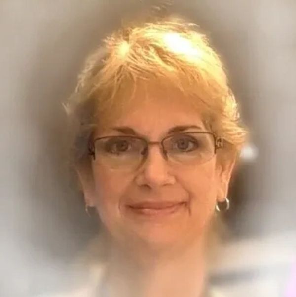 Portrait of a smiling middle-aged woman with glasses and short blonde hair.