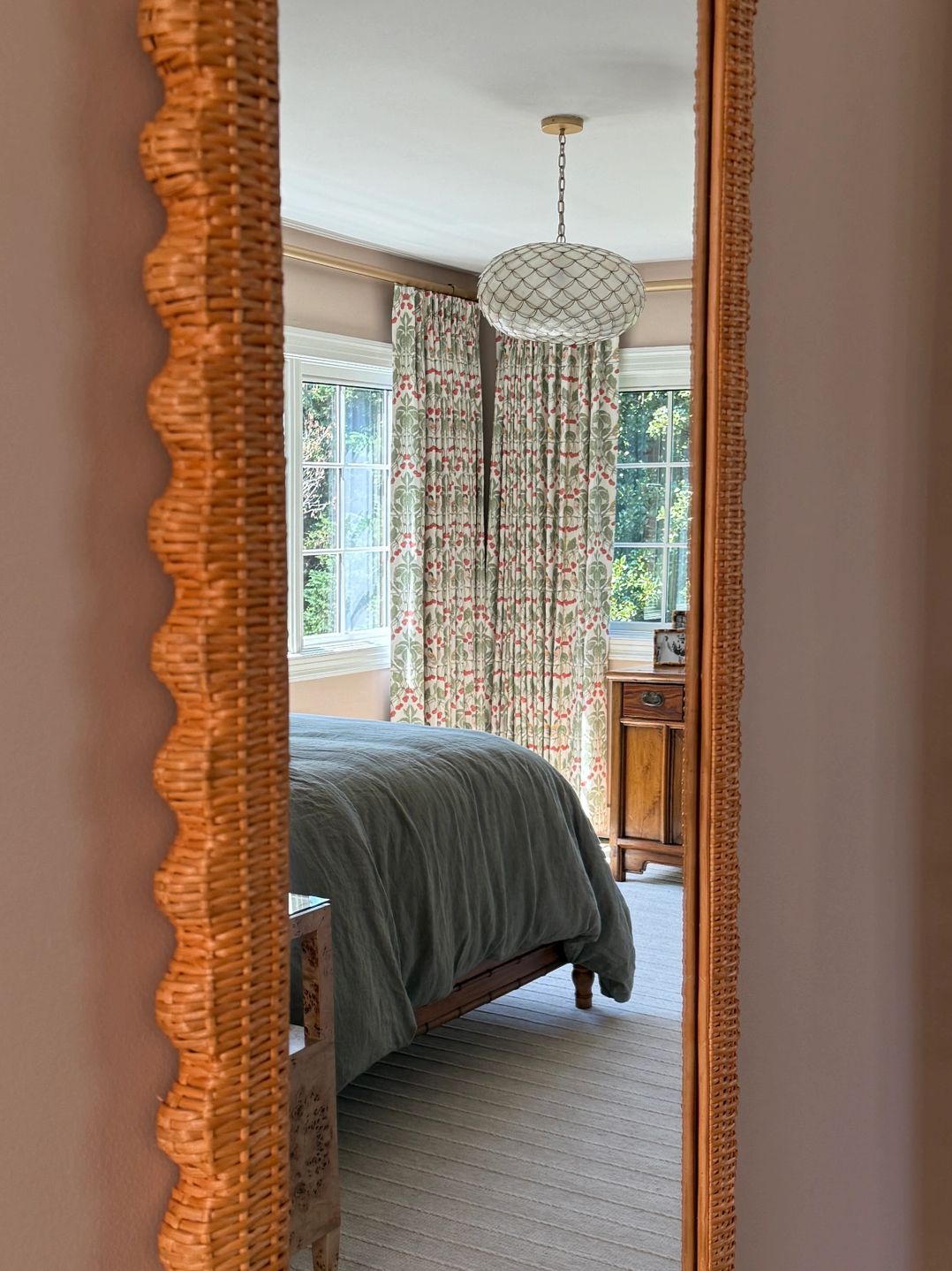 Rattan wall mirror reflecting bedroom with custom drapery