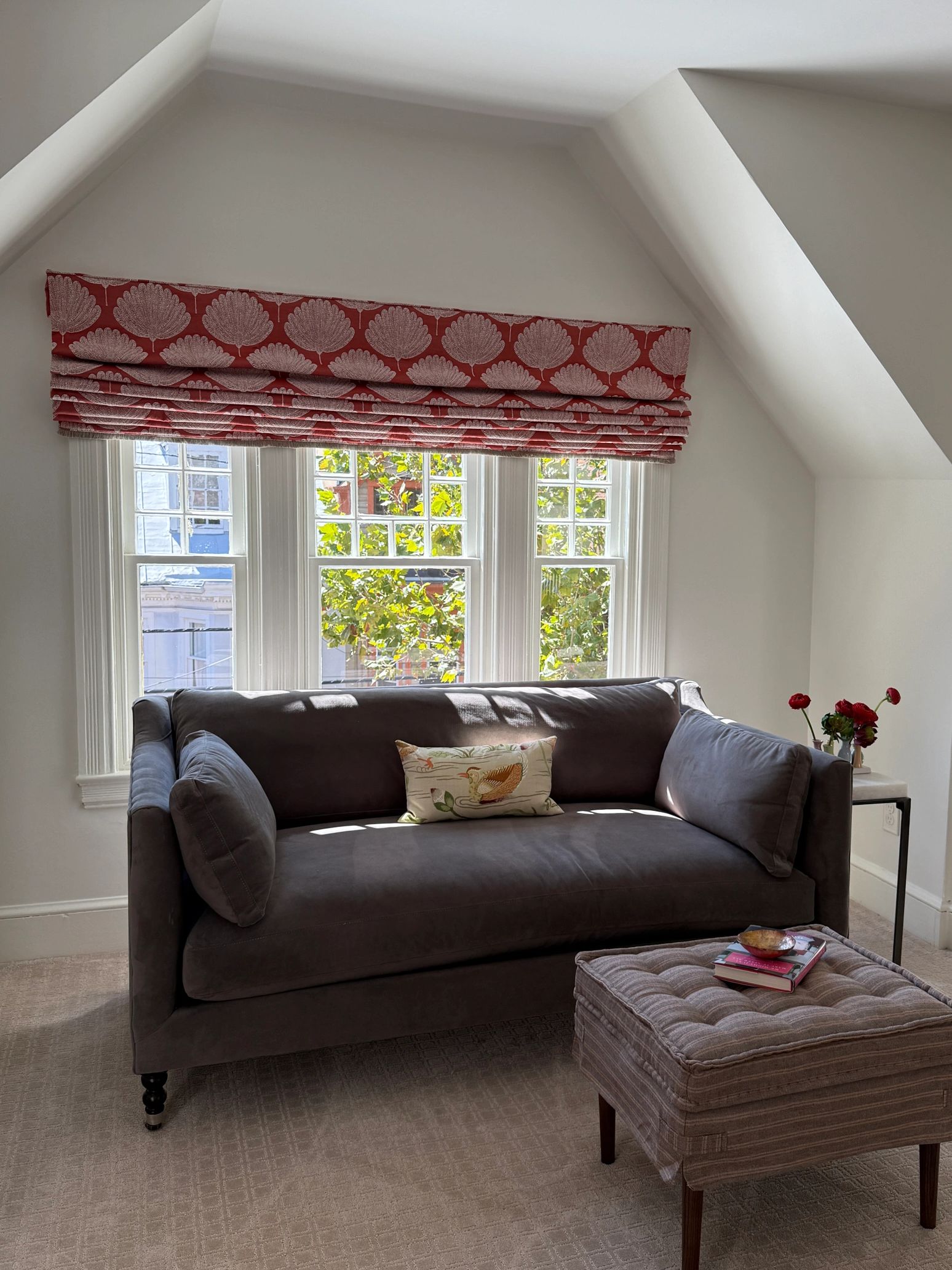 Velvet loveseat with square ottoman and roman shades in window