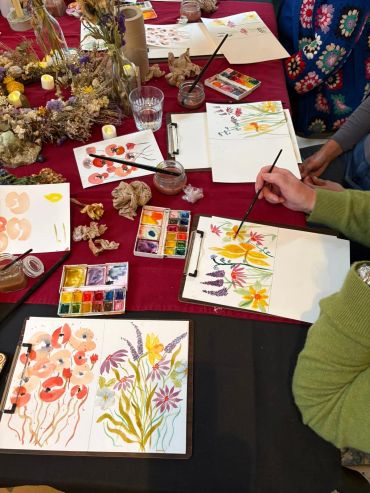 People painting colorful floral designs using watercolors at a table.