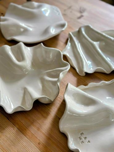 Four white ceramic dishes with organic, flowing shapes on a wooden surface.