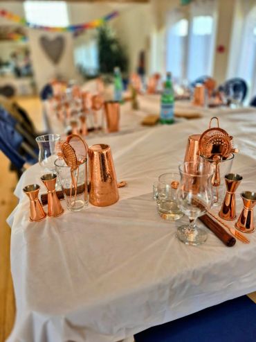 Copper bartending tools arranged on a table covered with a white cloth.
