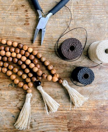 Crafting wooden bead garlands with tassels using pliers and string.