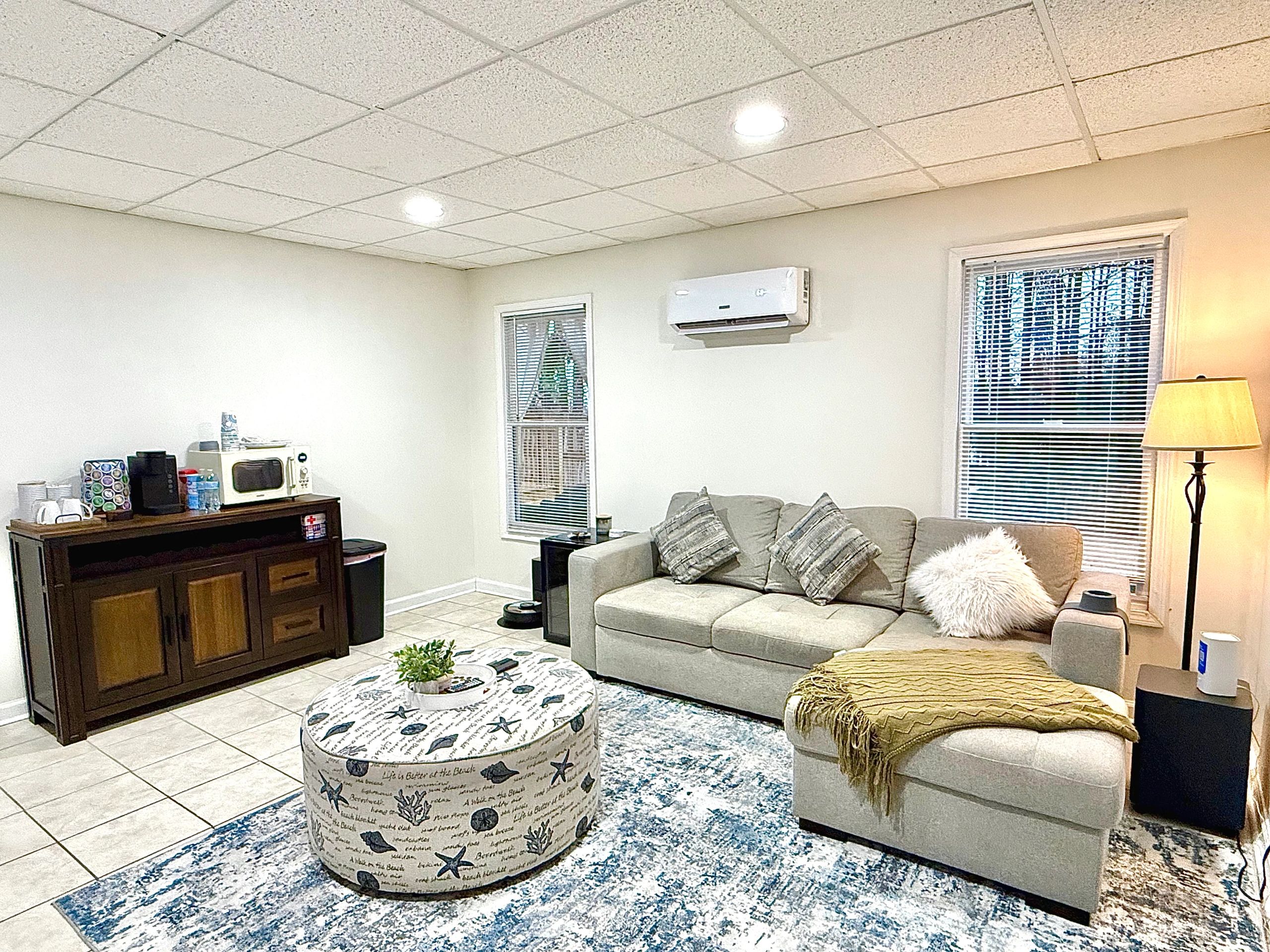 Cozy living room with gray sofa, patterned ottoman, and soft lighting.