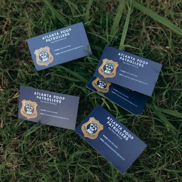 Business cards for Atlanta Poop Patrollers on grass, offering dog waste removal services.
