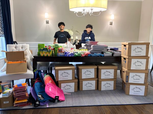 Two boys standing behind a table filled with school supplies and boxes.