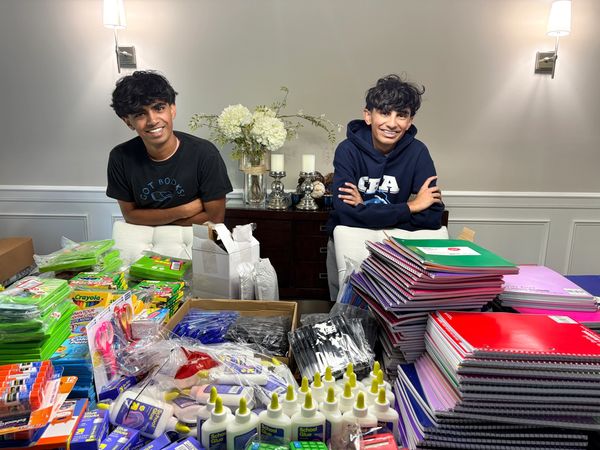 Two boys smiling behind a table full of school supplies.