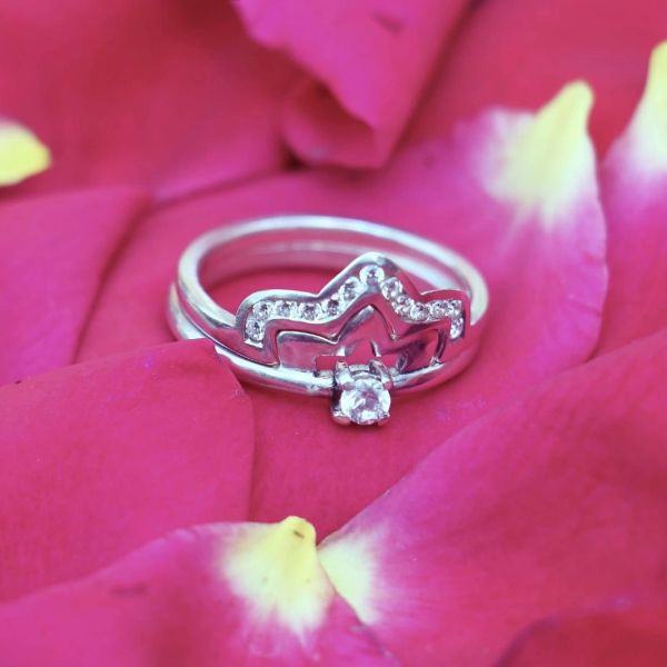 Silver crown-shaped ring on red rose petals.