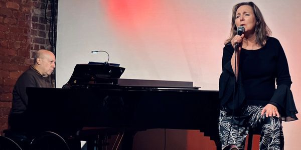 Woman singing with pianist on stage.