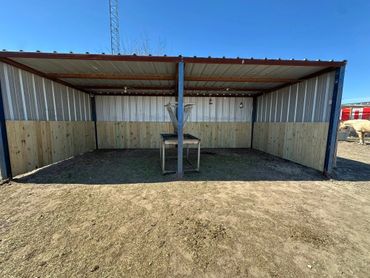Metal and wood animal shelter with feeding trough under clear blue sky.