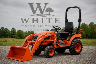 Orange Kubota BX2380 tractor with front loader on gravel near greenery.