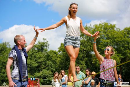 a very happy lady standing on a slackline supported by two of her friends