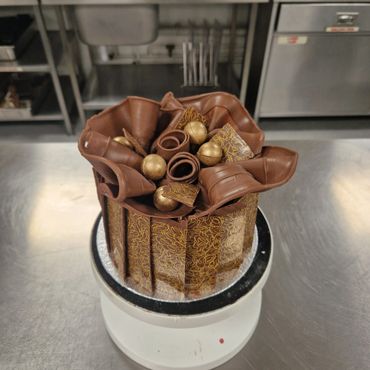 Elegant chocolate cake adorned with decorative chocolate curls and gold spheres.