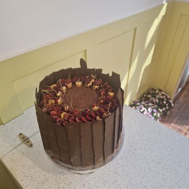 Chocolate cake decorated with cherries and chocolate panels on a white countertop.