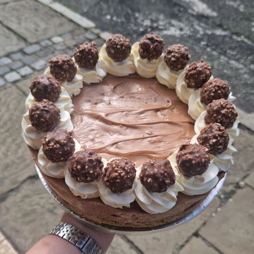 Hand holding a chocolate cake topped with cream and chocolate truffles.