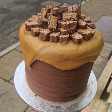 Hand holding a chocolate and caramel layered cake topped with chopped chocolate bars.