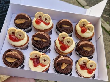 Box of assorted cupcakes with chocolate, peanut butter, and jam toppings.