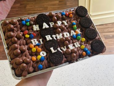 Chocolate birthday cake decorated with Oreos, colorful candies, and white letter toppers.
