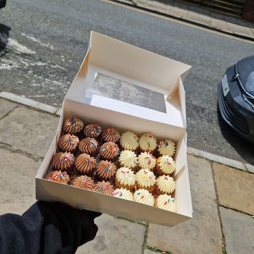 Box of assorted mini cupcakes with colorful sprinkles.