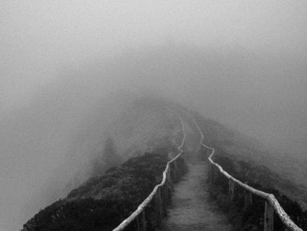 Foggy pathway on a mountain with wooden railings.