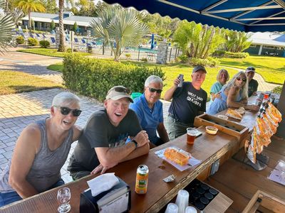 A group of seven adults enjoying drinks and snacks at an outdoor bar under an awning.