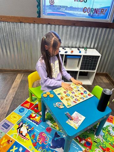 A girl playing with an alphabet puzzle at a colorful kids' corner table.