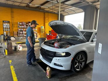 Mechanic inspecting a white car with its hood open in a garage.