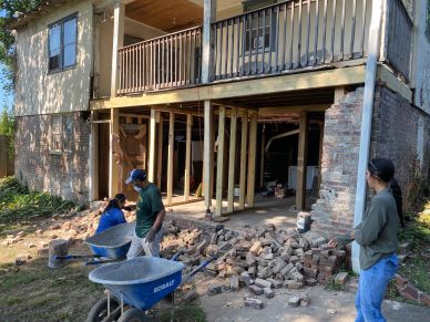 People working on house renovation with wheelbarrows and bricks.