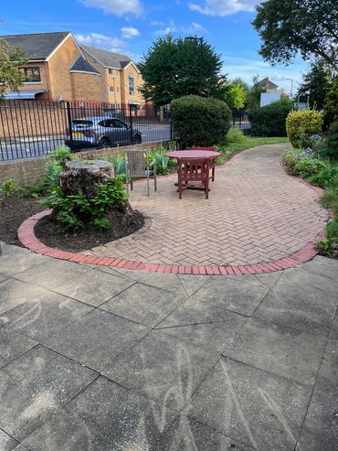 Concrete tiles and brick pathway surrounded by various green bushes, plants and trees