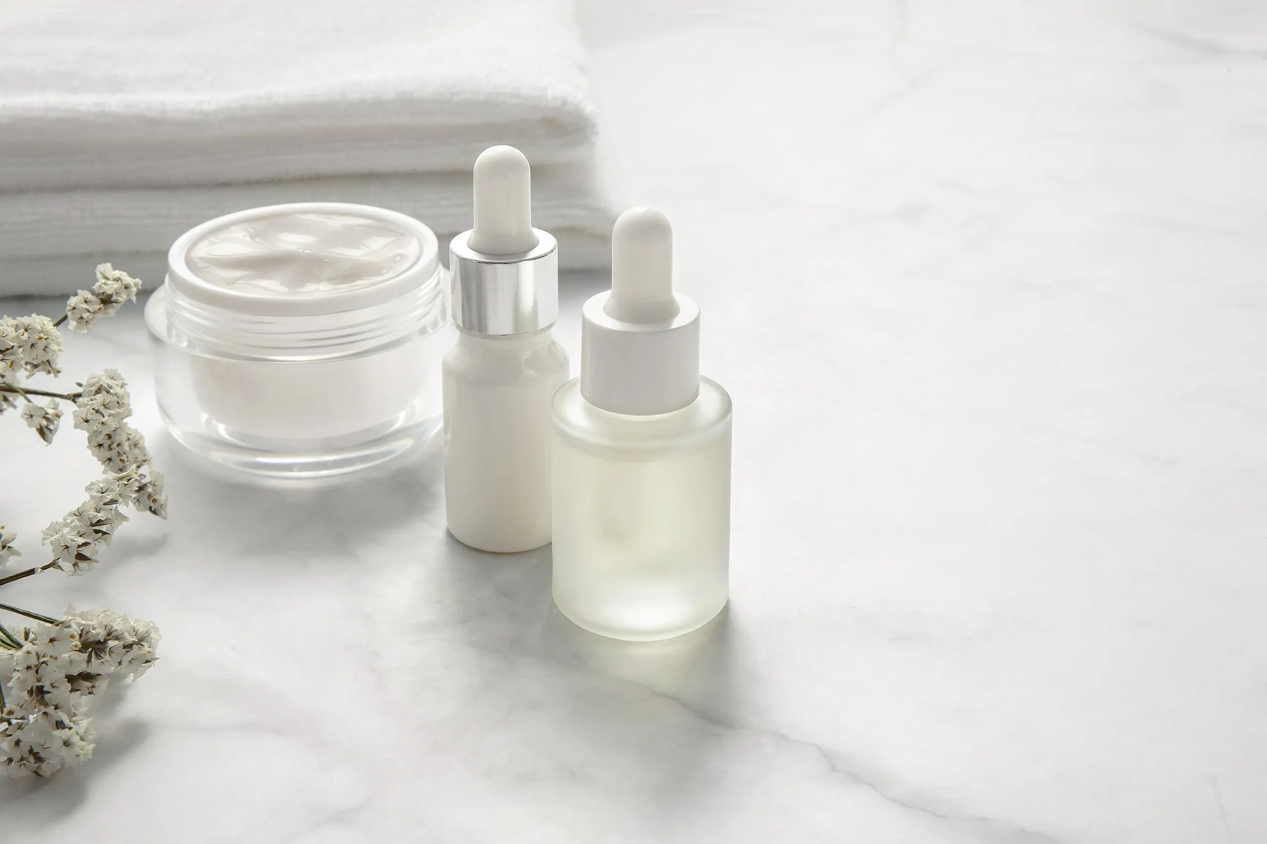 Minimalist skincare set with cream and serums on marble surface.