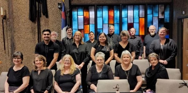 Group photo of 16 people inside a room with stained glass windows.