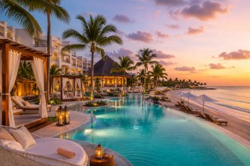 Luxurious beachside resort with pool at sunset and palm trees.