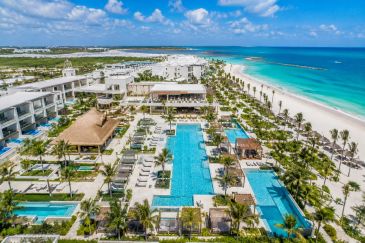A luxurious beachfront resort with pools and palm trees under a blue sky.