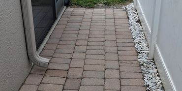 Narrow brick pathway between house and white fence with gravel border.