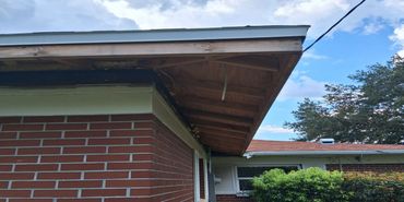 Brick house with exposed wooden roof rafters and a cloudy sky.