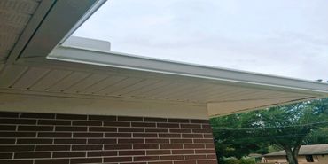 Brick wall with white eaves and a grassy yard under a cloudy sky.