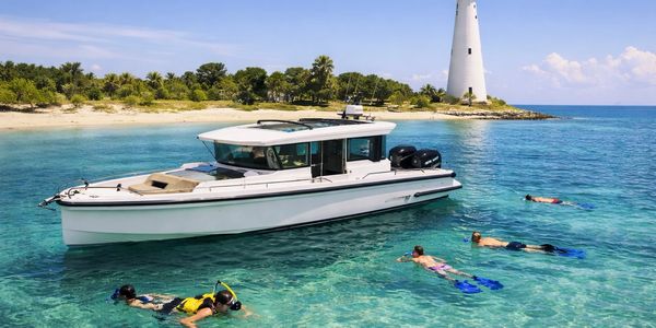 Snorkelers explore clear waters near a white yacht and lighthouse on a sunny day.