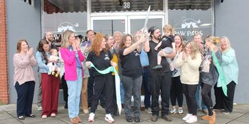 A group celebrating a ribbon-cutting event outside a business.