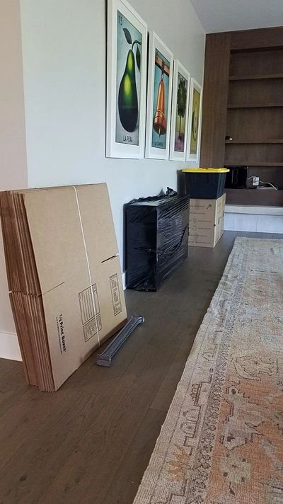 Flat cardboard and boxes on the floor of a living room with four pictures hanging on the wall