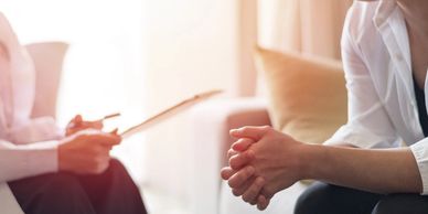 Two people in a counseling or therapy session, one holding a clipboard.