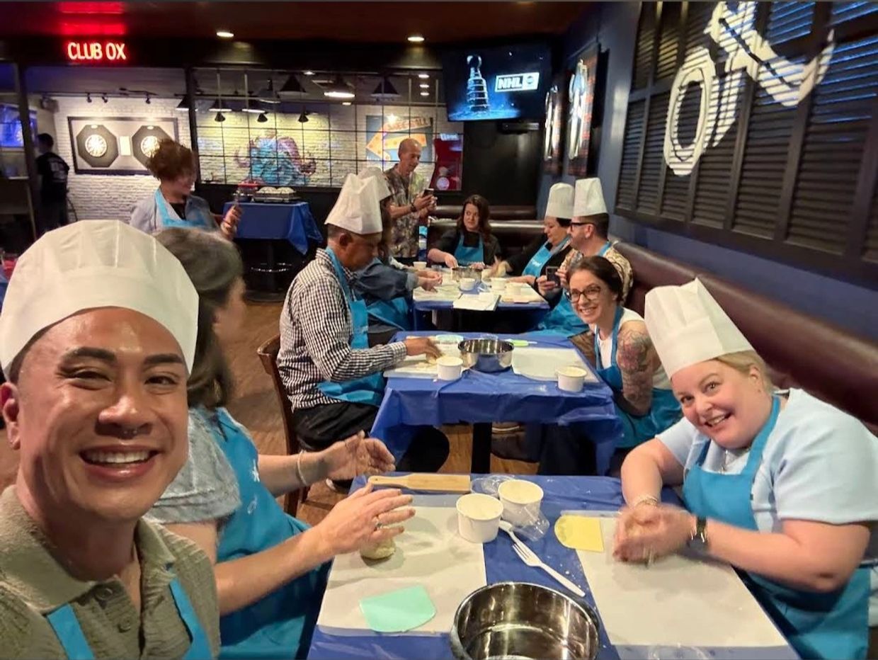 Group cooking class with participants in chef hats and blue aprons.