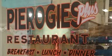 A chef statue holding a plate of fries in front of a pierogies restaurant window.