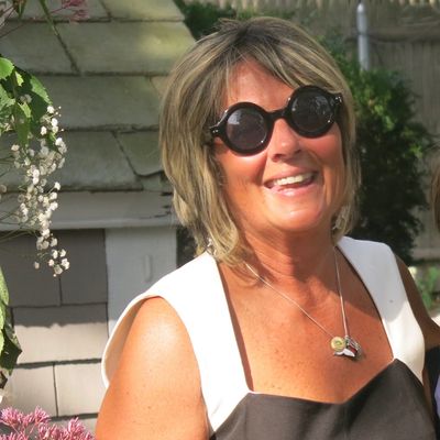 Woman smiling outdoors wearing round black sunglasses.