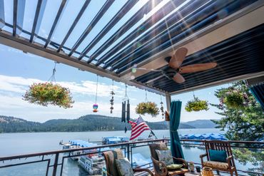 Balcony overlooking a serene lake with hanging plants and a ceiling fan.
